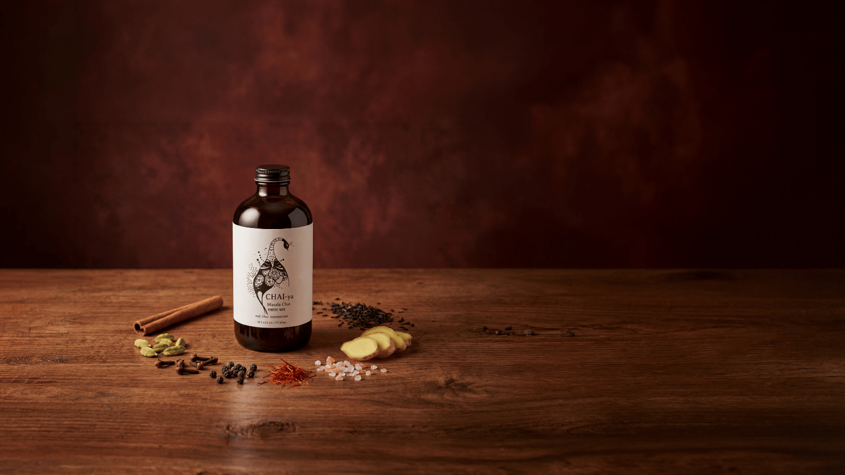 Masala chai concentrate bottle with traditional Indian spices – cinnamon, cardamom, cloves, ginger, black pepper, and saffron on rustic brown surface